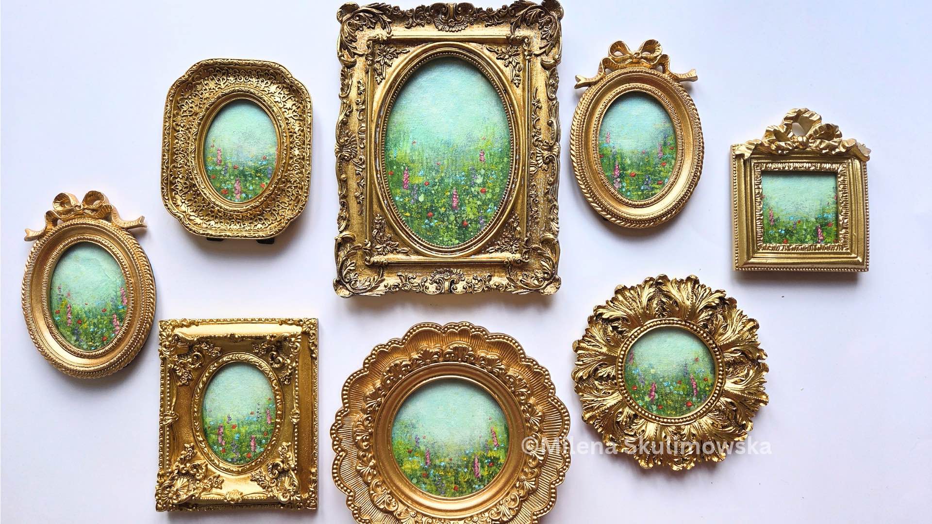 Collection of miniature impressionist meadow paintings in ornate gold frames, arranged on a white background, each showing a soft blue-green sky above a green field with small colourful flowers.