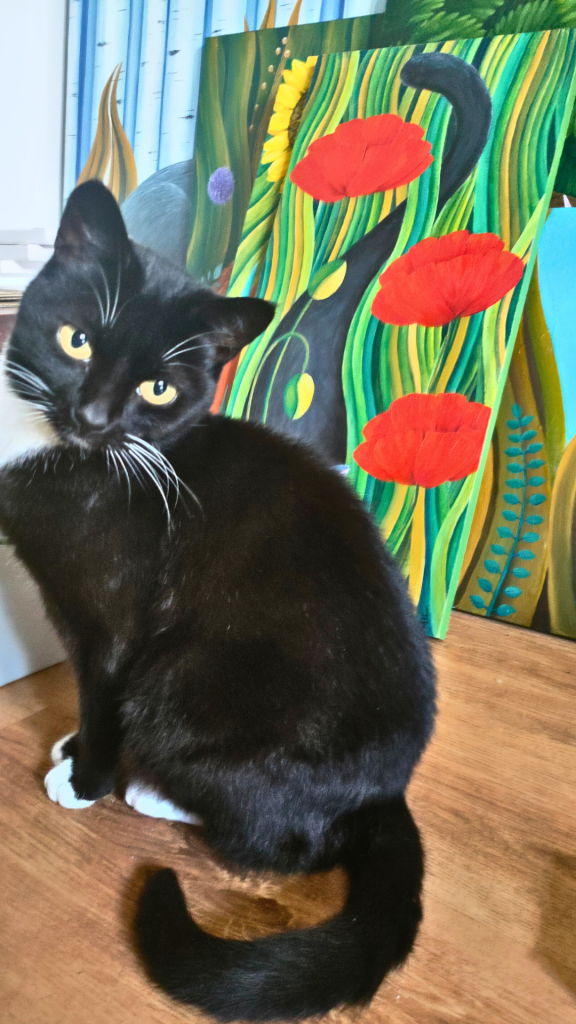 A black cat with striking golden eyes sits elegantly on a wooden floor against a vibrant painting background. The painting features bright red poppies and green foliage on a turquoise background. The cat's fur is glossy black, and it has distinctive white paws. The composition captures the intersection of feline grace and artistic creativity in a studio setting.