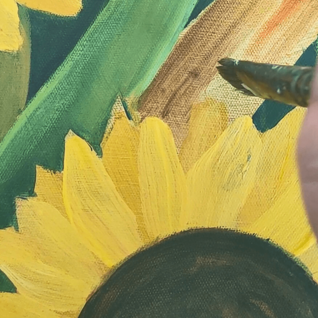 Close-up of an acrylic painting in progress, showing bright yellow sunflower petals contrasting with deep green foliage. A brush is visible adding details to the flowing organic shapes on canvas texture.