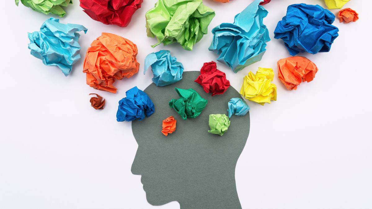 Silhouette of a head cut-out on a white background with colourful crumpled paper balls above it, suggesting busy or overwhelming thoughts.