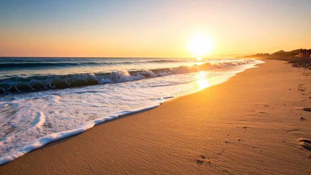 Sunrise over a sandy beach with gentle waves, a bright sun near the horizon, and a warm golden reflection across the shoreline.